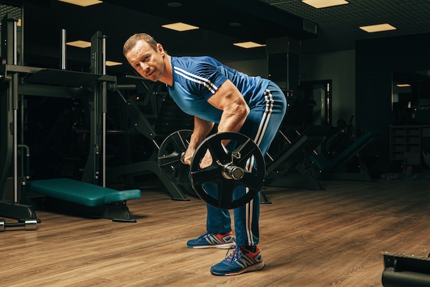 Fit elderly man lifting barbell in a gym