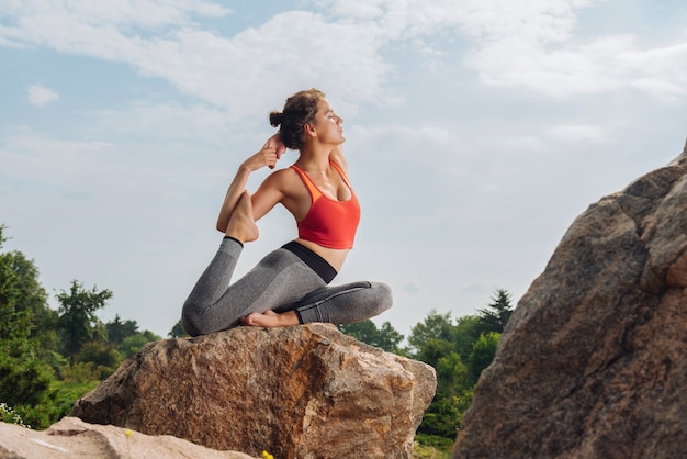 Fit en slank ervaren yogavrouw die yoga asana toont terwijl ze op een rots in het bos zit