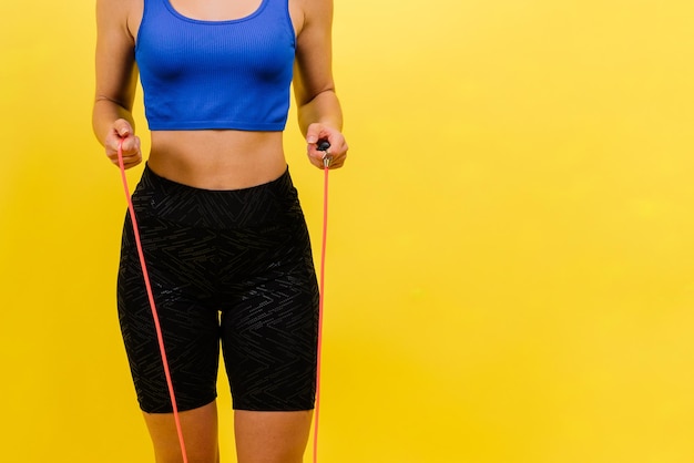 Fit female athlete with ponytail jumping with rope during fitness training against yellow background