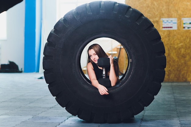Photo fit female athlete working out with a huge tire turning and carry in the gym woman exercising with