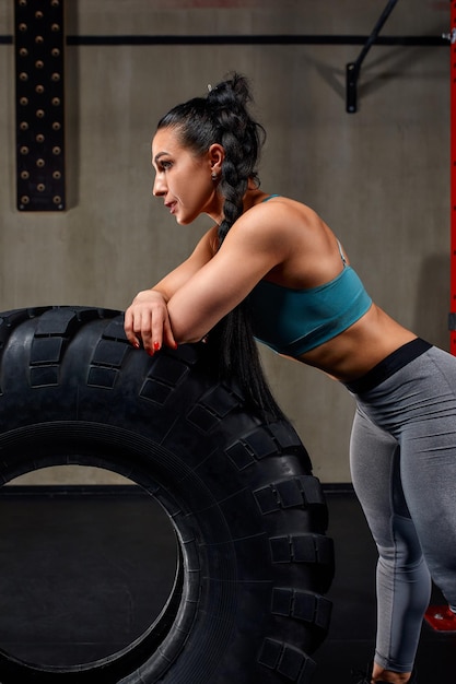 Fit female athlete working out with a huge tire turning and flipping in the gym Crossfit woman exercising with big tire