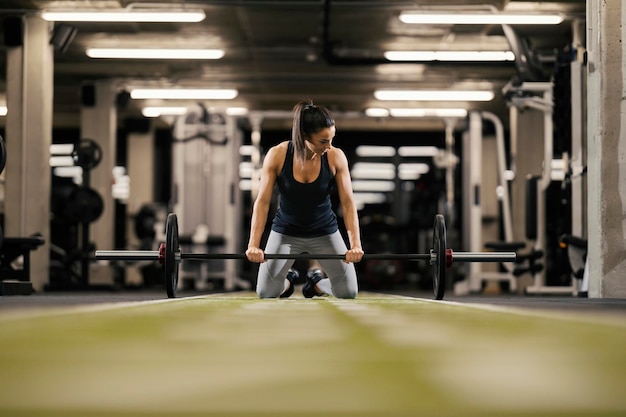 A fit female bodybuilder is preparing to lift barbell in a gym