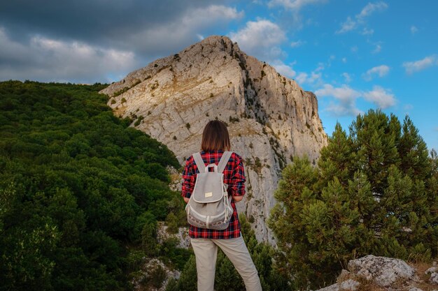 Подходит женщина-туристка с рюкзаком, стоящая на скалистом горном хребте