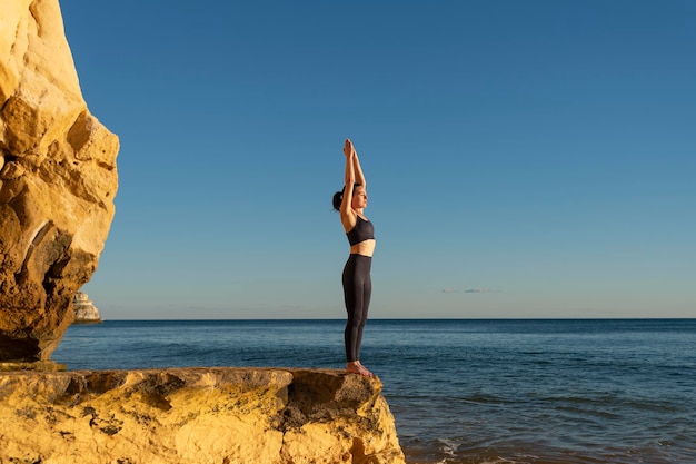 Foto donna in forma che pratica yoga su una roccia vicino al mare