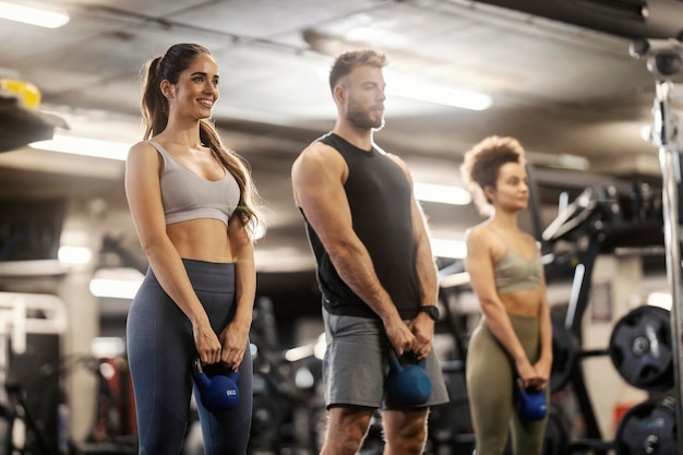 Fit friends in shape standing in a gym and exercising with kettlebells