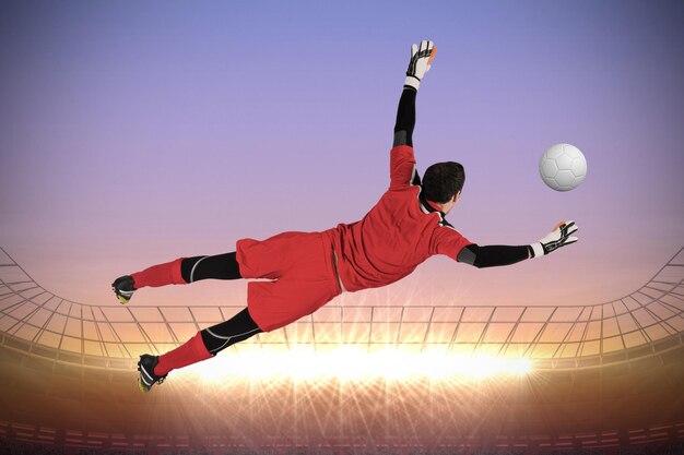 Photo fit goal keeper jumping up against large football stadium with spotlights at sunrise