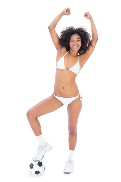 Fit happy girl in white bikini holding football at her foot