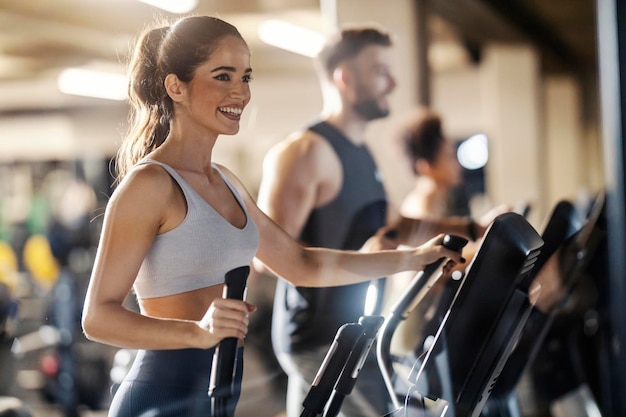 Photo fit happy sportswoman is exercising with her friends on synchro machine in a gym