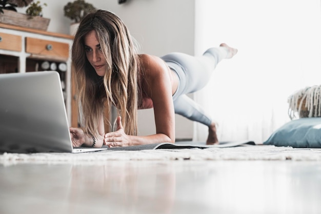 Fit and healthy lifestyle young woman doing plank position at home looking a lesson on the laptop Sport and active workout on the web Following internet channel about body positivity and health