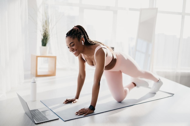 Fit jonge Afro-Amerikaanse vrouw met koptelefoon doen krachttraining voor laptop thuis