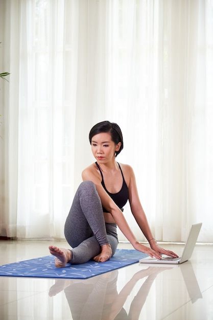 Fit jonge Aziatische vrouw die zittende spinale twist doet om te oefenen bij het werken op laptop