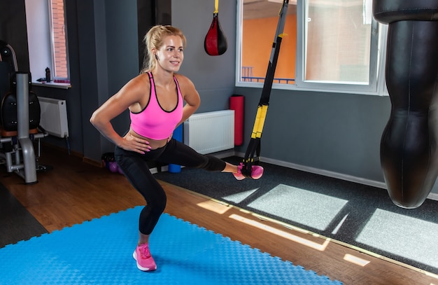 Fit jonge blonde vrouw trainen met fitness TRX bandjes in de sportschool. Fitnesstraining voor vrouwelijk lichaam