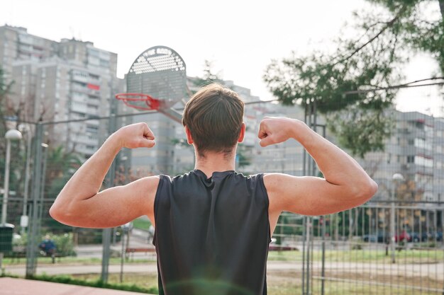 Fit jonge man in sportkleding doet het sterke gebaar op een basketbalveld