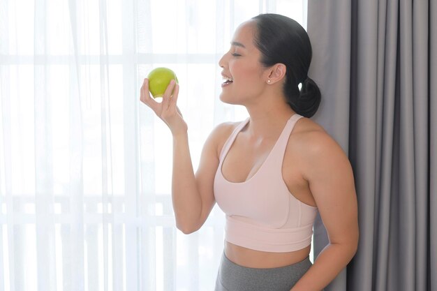 Fit jonge vrouw die een appel eet na thuis sporten en een gezond levensstijlconcept