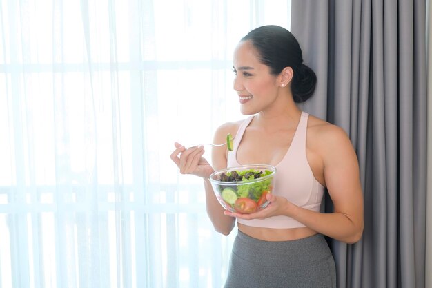 Fit jonge vrouw met salade na thuis sporten en gezonde levensstijl concept