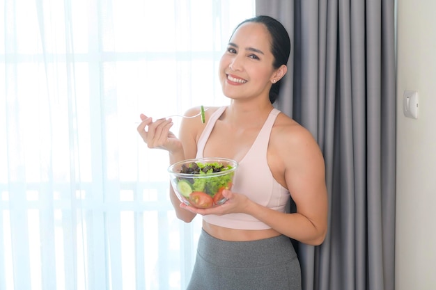 Fit jonge vrouw met salade na thuis sporten en gezonde levensstijl concept