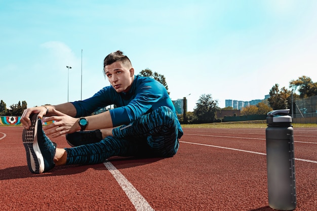 The fit male runner stretching legs preparing for run during training at stadium tracks. The athlete, fitness, workout, sport, exercise, training, athletic, lifestyle concept