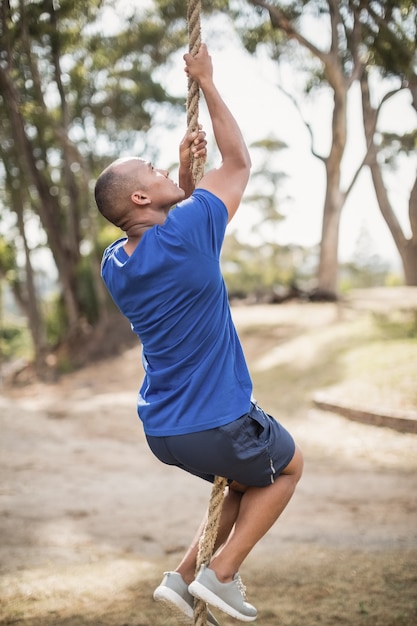 Fit man climbing rope during obstacle course in boot camp