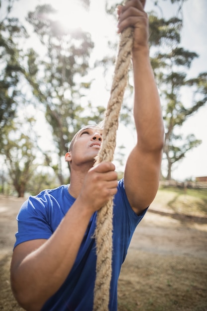 Fit man climbing rope during obstacle course in boot camp