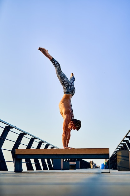 Fit man doet een handstand terwijl hij alleen yoga beoefent in de buurt van de oceaan tegen de lucht in de schemering of zonsopgang