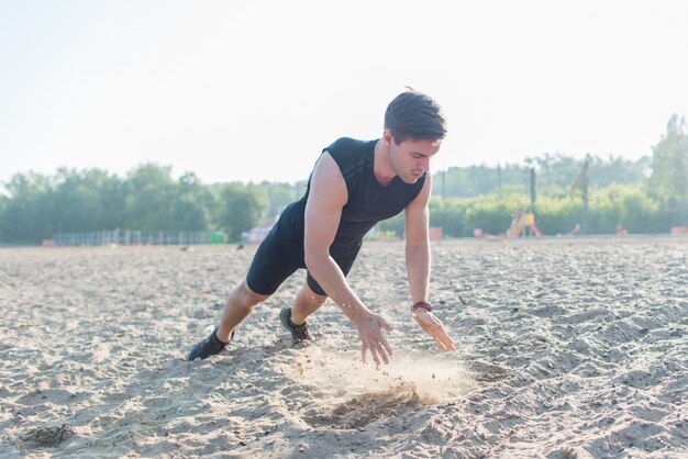 Fit man doing clapping push-ups during training exercise workout on beach in summer.