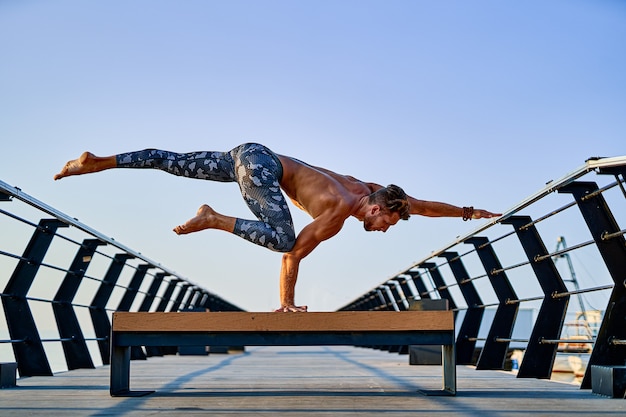 Foto uomo in forma che fa una mano mentre pratica yoga da solo vicino all'oceano contro il cielo al tramonto o all'alba