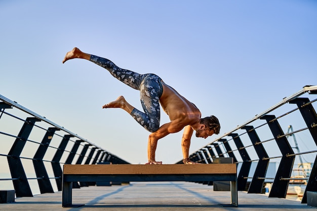 Foto uomo in forma che fa una mano mentre pratica yoga da solo vicino all'oceano contro il cielo al tramonto o all'alba