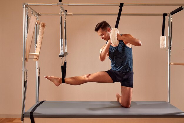 Fit man doing a lunge stretch yoga pilates exercise to strengthen and tone his muscles using a reformer in gym Health and fitness concept