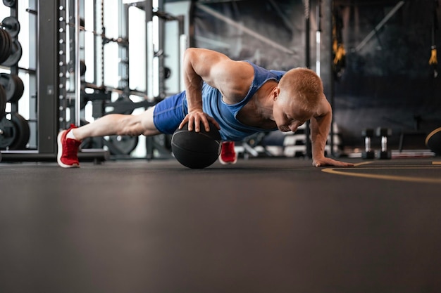 Photo fit man doing push ups on medicine ball at the gym