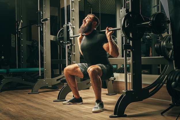 Fit man doing squats in a training machine