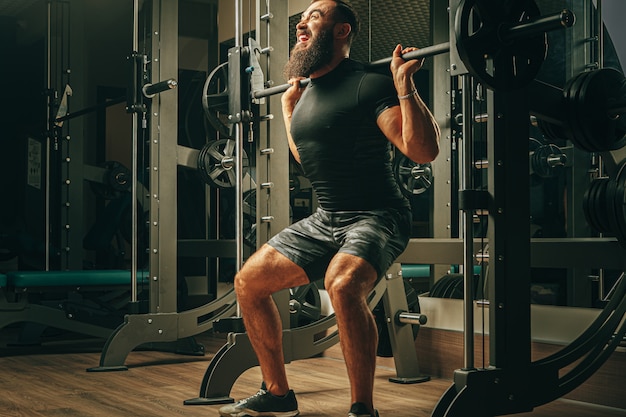 Fit man doing squats in a training machine