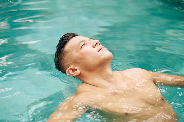 スイミングプールで背中に浮かんで空を見ている男に合う