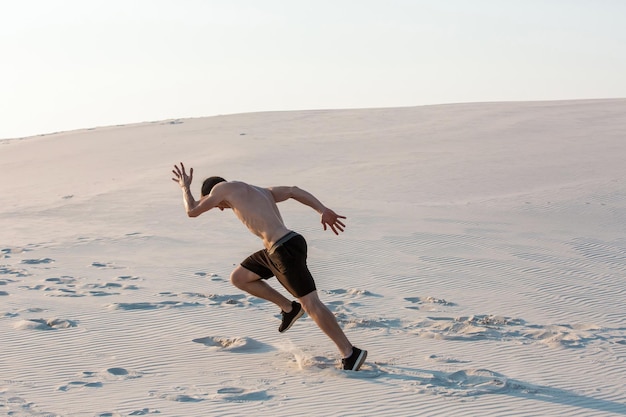 Fit man loopt snel op het zand. Krachtige hardloper die in de zomer buiten traint.