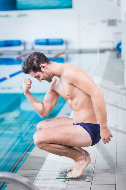 Fit man triomfeert op de weging schaal bij het zwembad