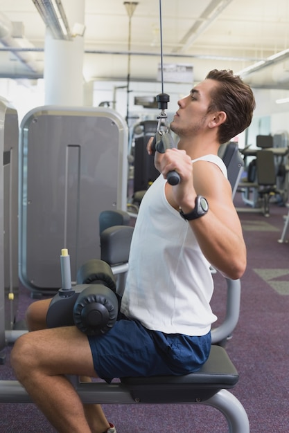 Fit man using the weights machine for his arms 