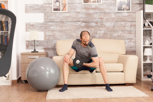 Fit man workout out his biceps with dumbbells at home during covid-19 self isolation.