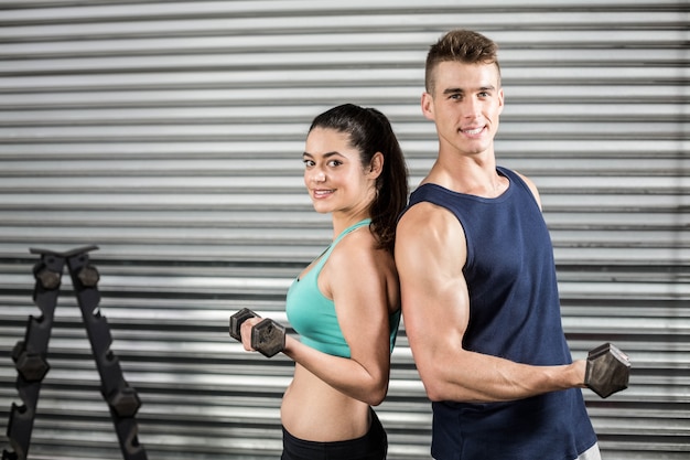 Fit mensen tillen dumbbells rug aan rug in de sportschool