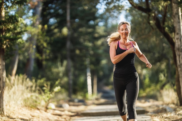 Fit middle age women are jogging through the pine forest near sea shore and enjoying in summer sunny day.