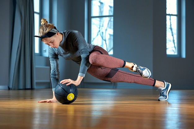 Fit and muscular woman doing intense core workout with kettlebell in gym. Female exercising at crossfit gym.