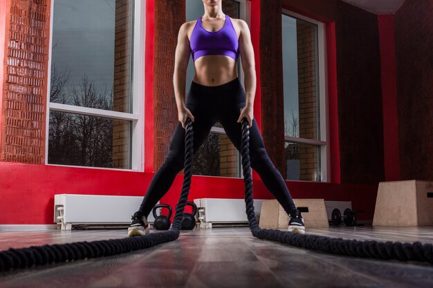 Fit and muscular woman exercising with battling ropes at fitness