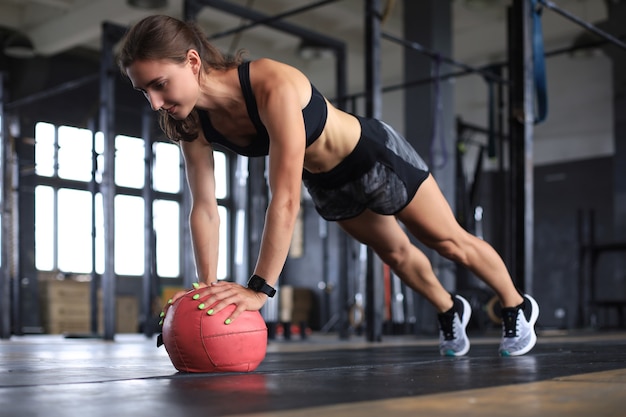 Fit and muscular woman exercising with medicine ball at gym.