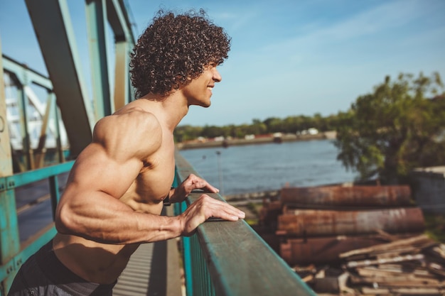 筋肉質の若い男性ランナーに、橋の上で腕立て伏せをしている裸の胴体を装着します。