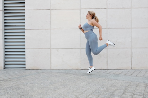 朝に屋外でジョギングする灰色のスポーツウェアのプラスサイズの若い女性にフィット