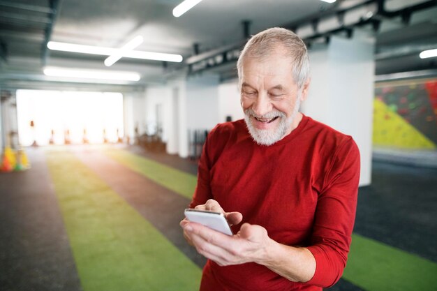 Fit senior man with smart phone in gym