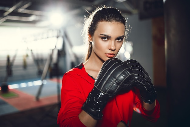 Giovane bella donna castana esile adatta che inscatola in abiti sportivi. luce fioca scura.