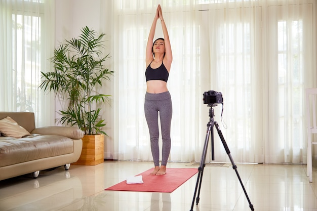 Fit slim young woman filming herself doing sun salutation yoga practice