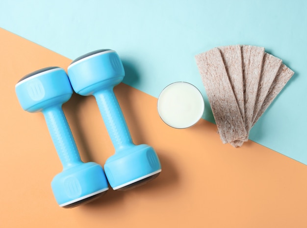 Fit slimming concept. Dumbbells, glass of kefir, diet crispbread on a blueorange