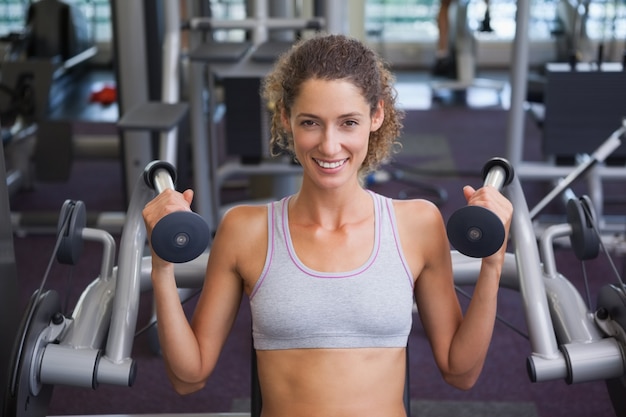 Fit smiling woman using the weights machine for her arms 