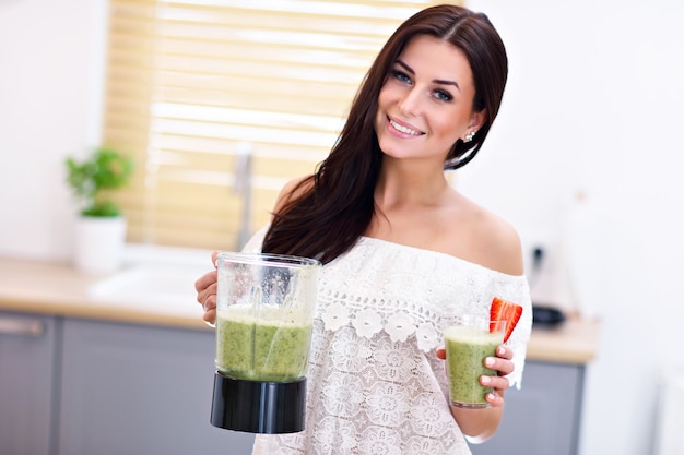 fit smiling young woman preparing healthy smoothie in modern kitchen