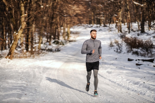 Fit sportman die in het bos loopt op een zonnige besneeuwde winterdag. Buitenfitness, cardio-oefeningen, winterfitness